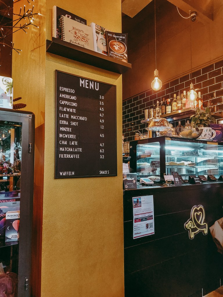 Drinks menu and glass display counter inside Dieter’s Café, illuminated by warm pendant lights.