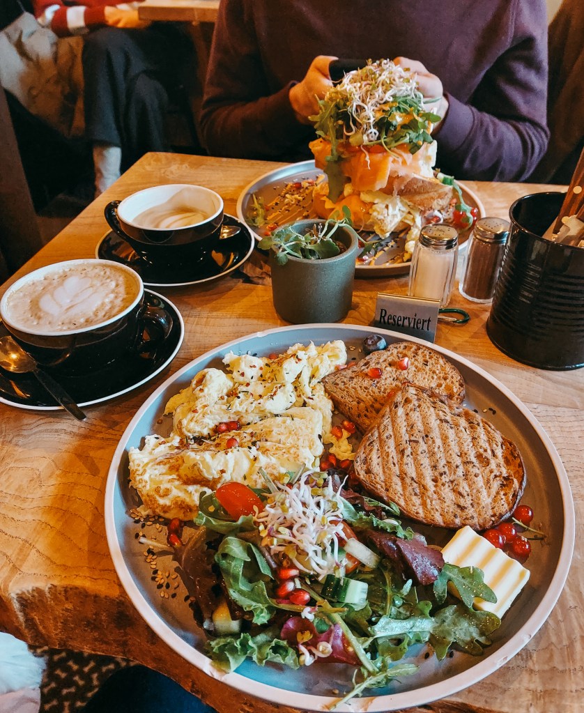 Two generous brunch dishes at Dieter’s Café: scrambled eggs with bread and salad, and a towering salmon brioche.