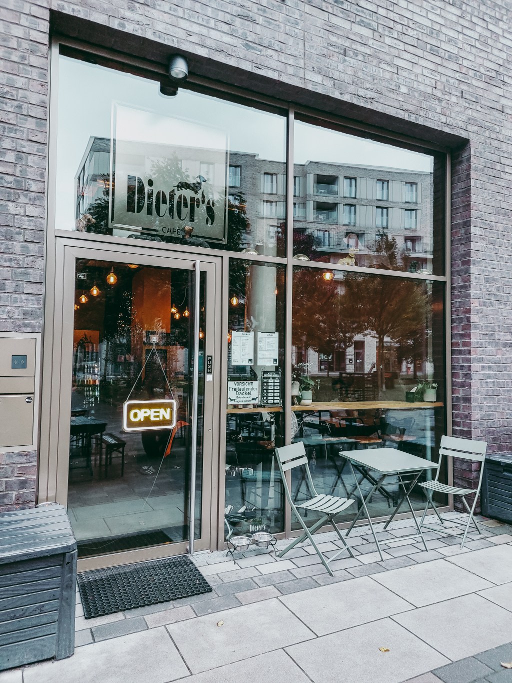 Entrance to Dieter’s Café in Hamburg-Altona, with its window logo and a small outdoor table and chairs.